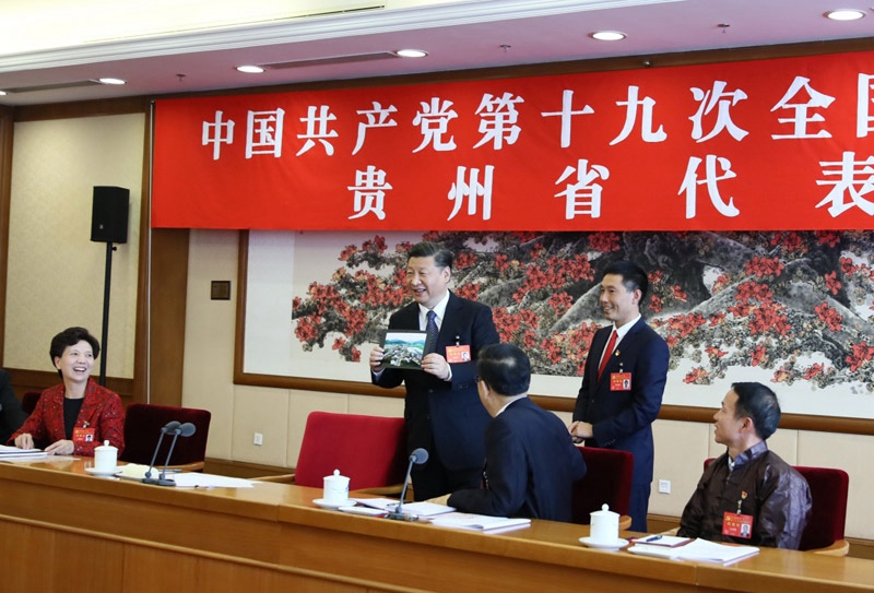 10月19日，習近平同志參加黨的十九大貴州省代表團討論。這是遵義市播州區花茂村黨總支書記潘克剛將一幅鳥瞰村子新貌的照片送到習近平面前。習近平起身接過照片，邊看邊稱贊：“這是風景畫，很漂亮！”新華社記者 蘭紅光 攝